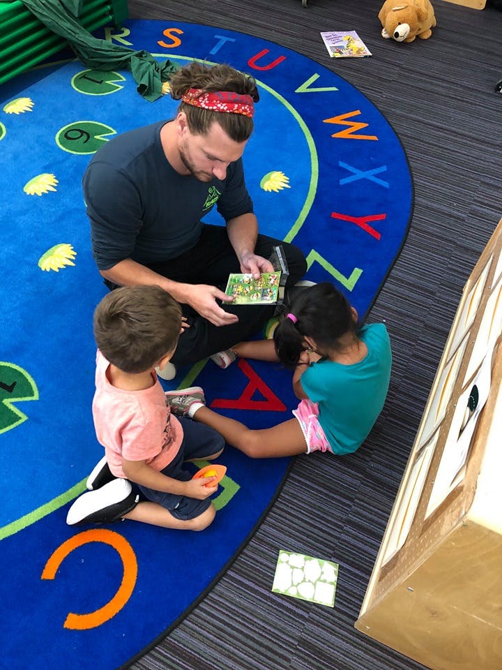 Person reading a book to two children on an alphabet rug