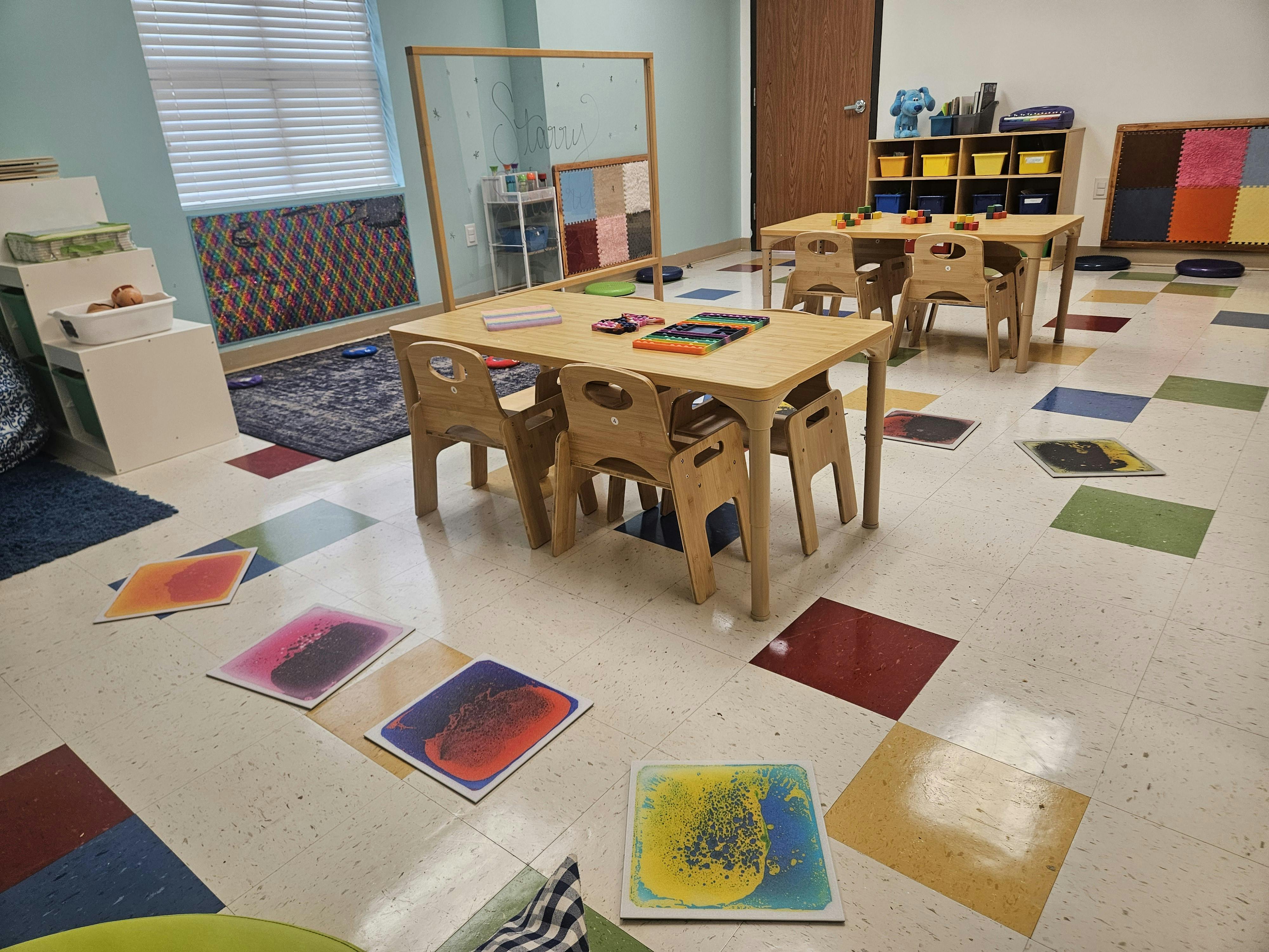 Classroom with small wooden tables and chairs, colorful mats on the floor
