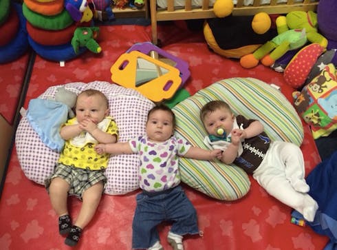 Three babies lying on pillows on a red floor