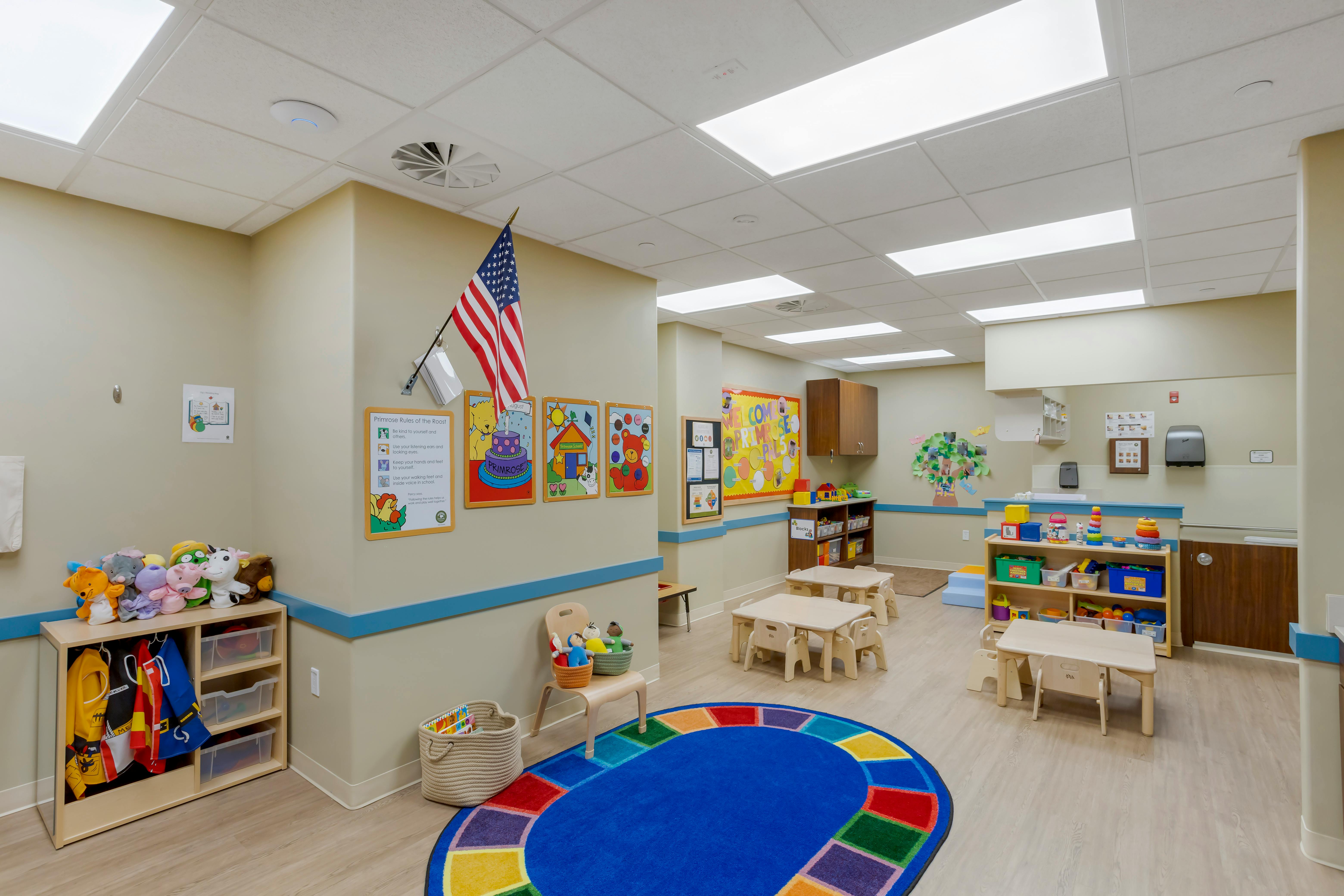 An empty early childhood classroom with small tables, chairs, and play areas