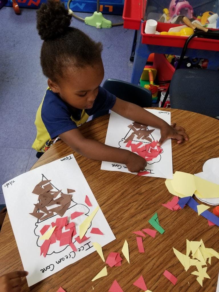 Child making an ice cream cone craft with paper cutouts