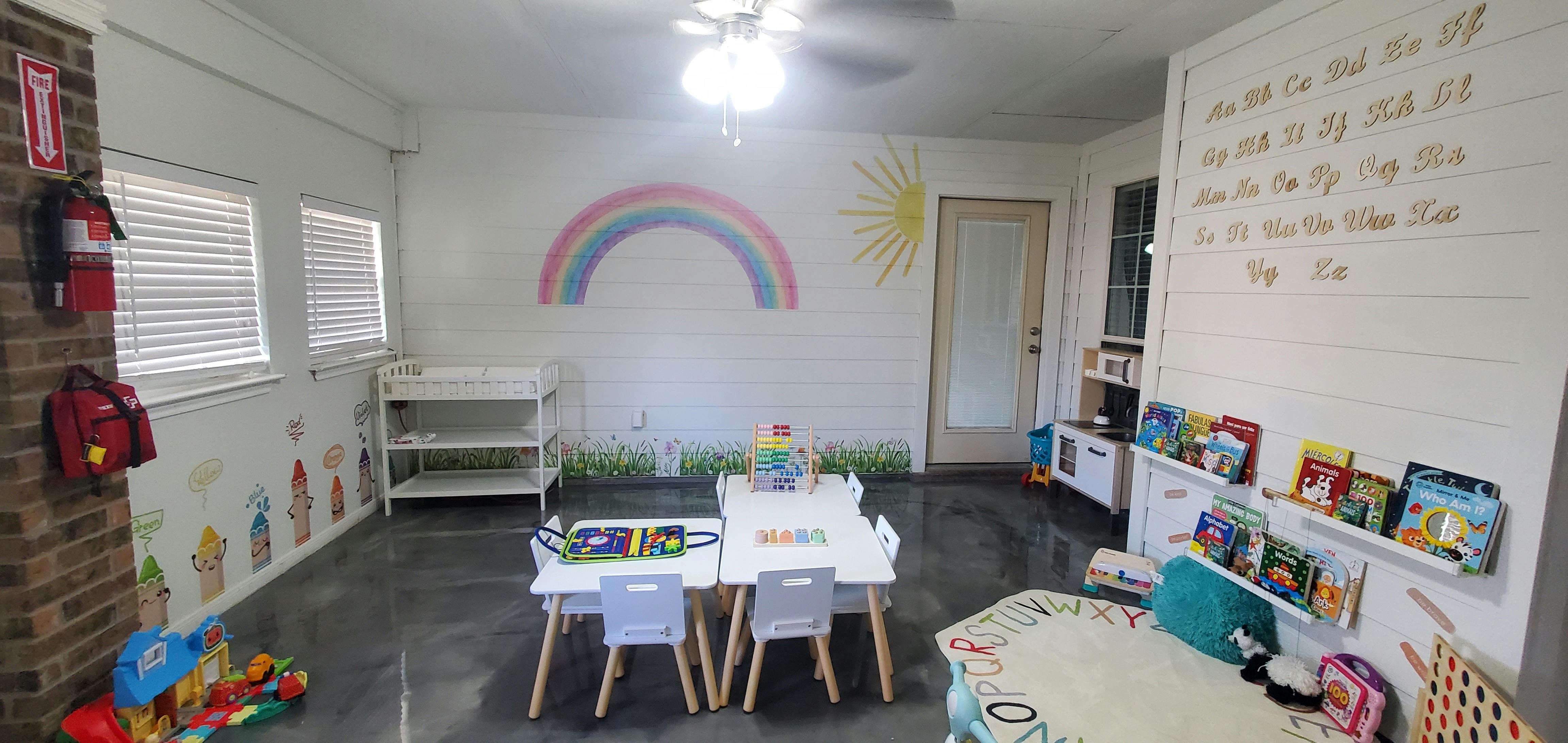 Classroom with small tables and chairs, rainbow and sun mural on wall