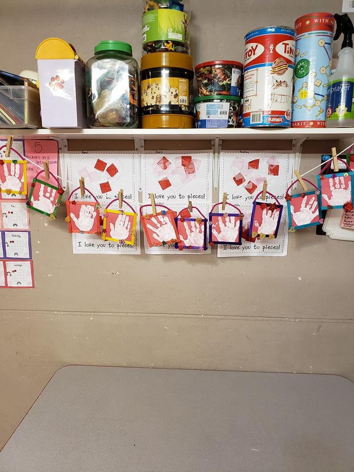 Child handprint crafts hanging on a string below a shelf with various containers