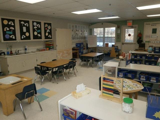 Empty classroom with small tables and chairs, sink, and learning materials