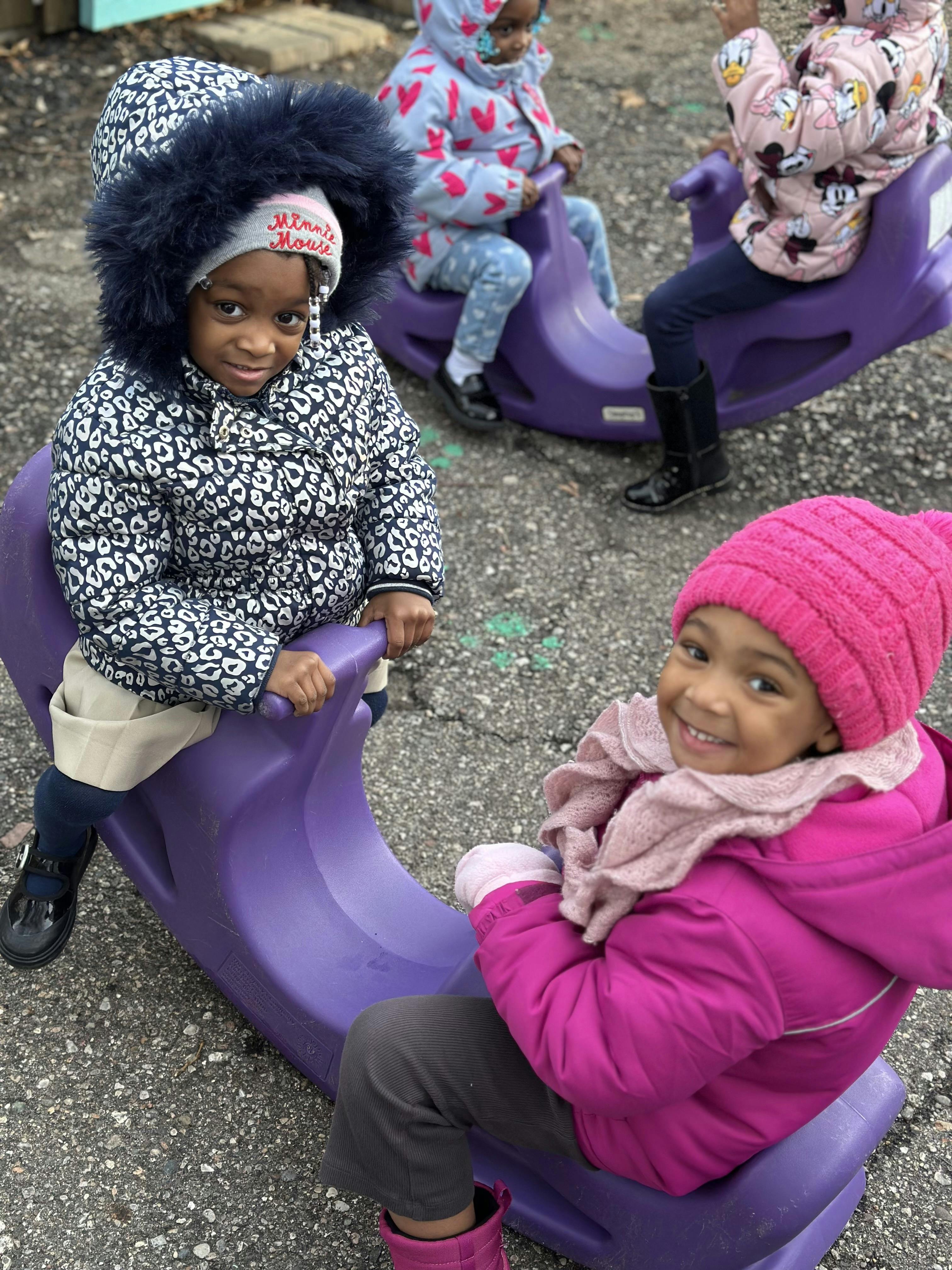 Children sitting on purple outdoor rocking toys