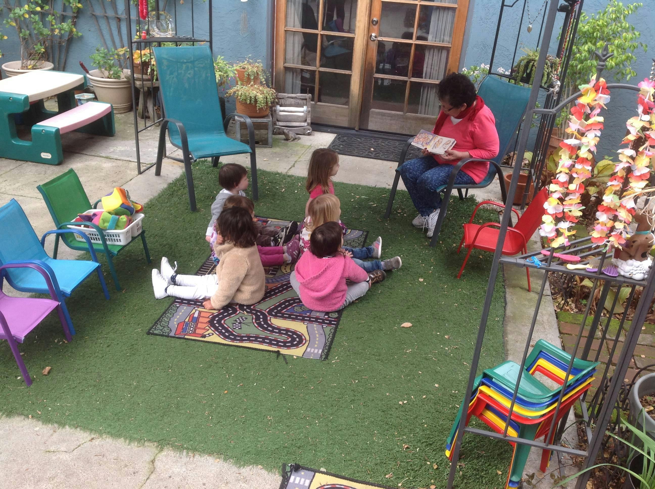 Person reading to children sitting on a rug outdoors