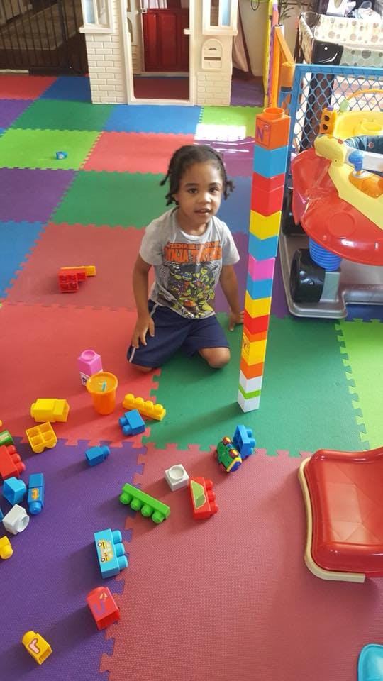 Child kneeling on a colorful playmat next to a tall stack of building blocks