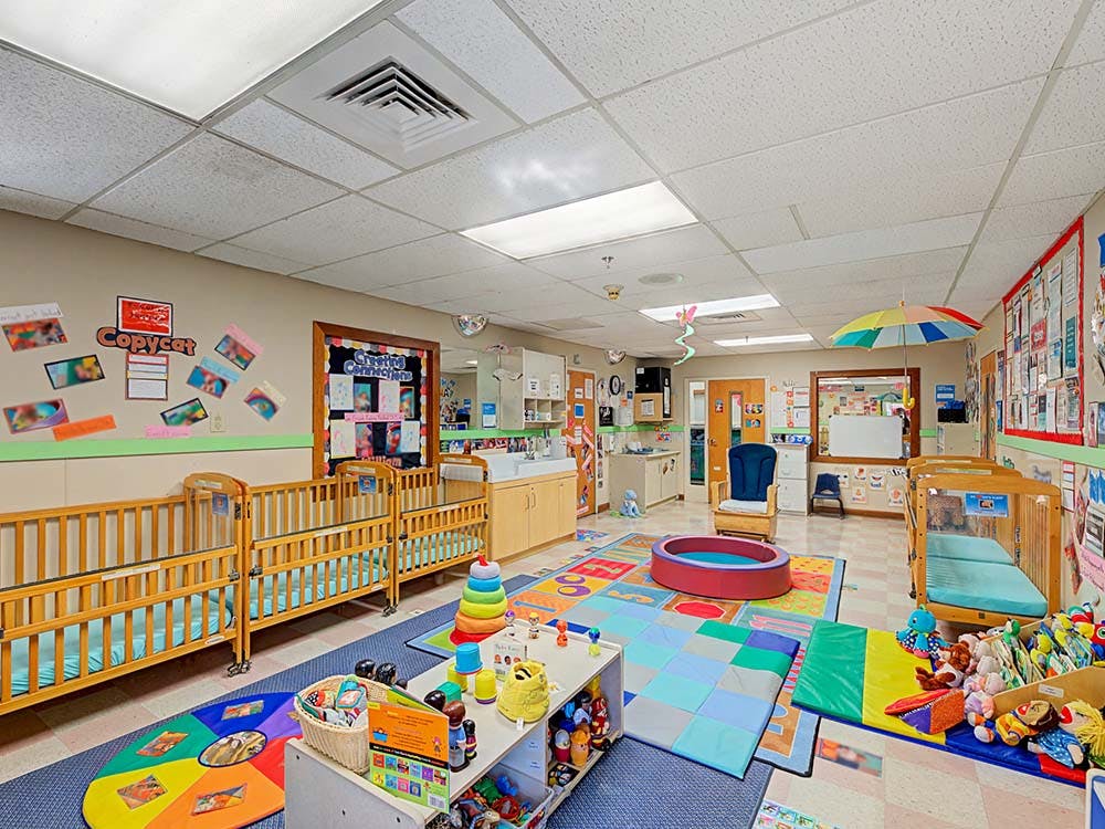 daycare classroom with multiple cribs, play mats, and toys