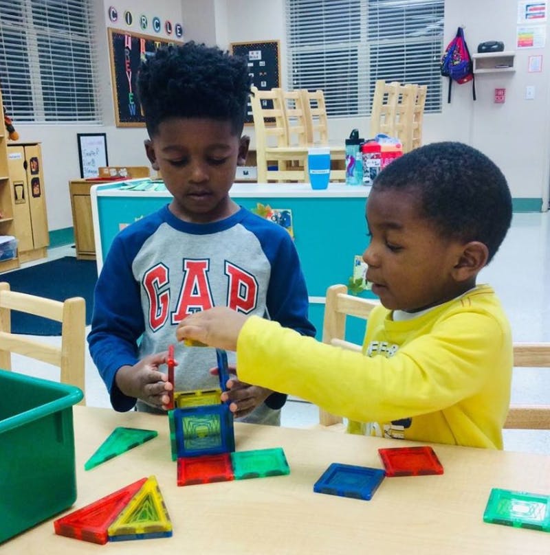 Two children playing with colorful magnetic building tiles at a table in a classroom