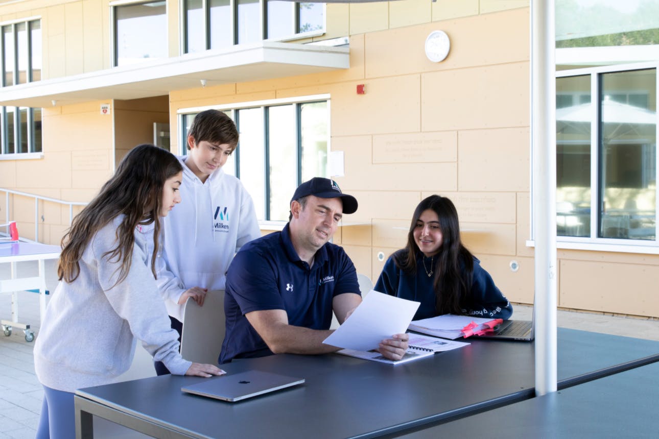 Adult and three teens looking at papers at an outdoor table