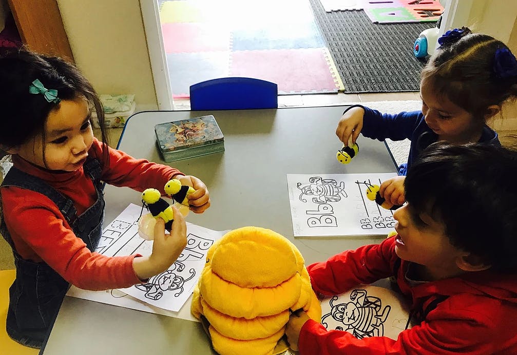 Three children playing with bee toys and coloring pages at a table