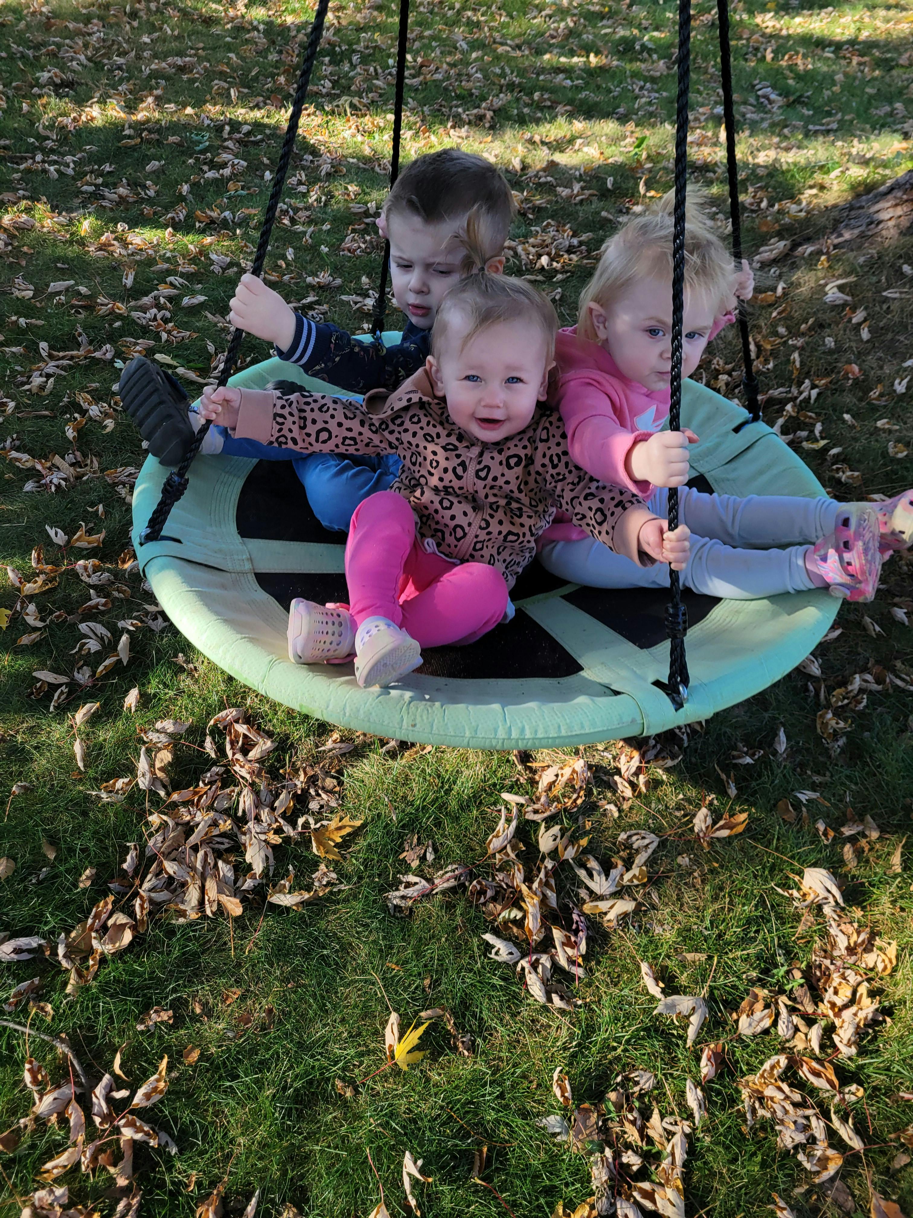 Three children sitting in a large green swing outdoors