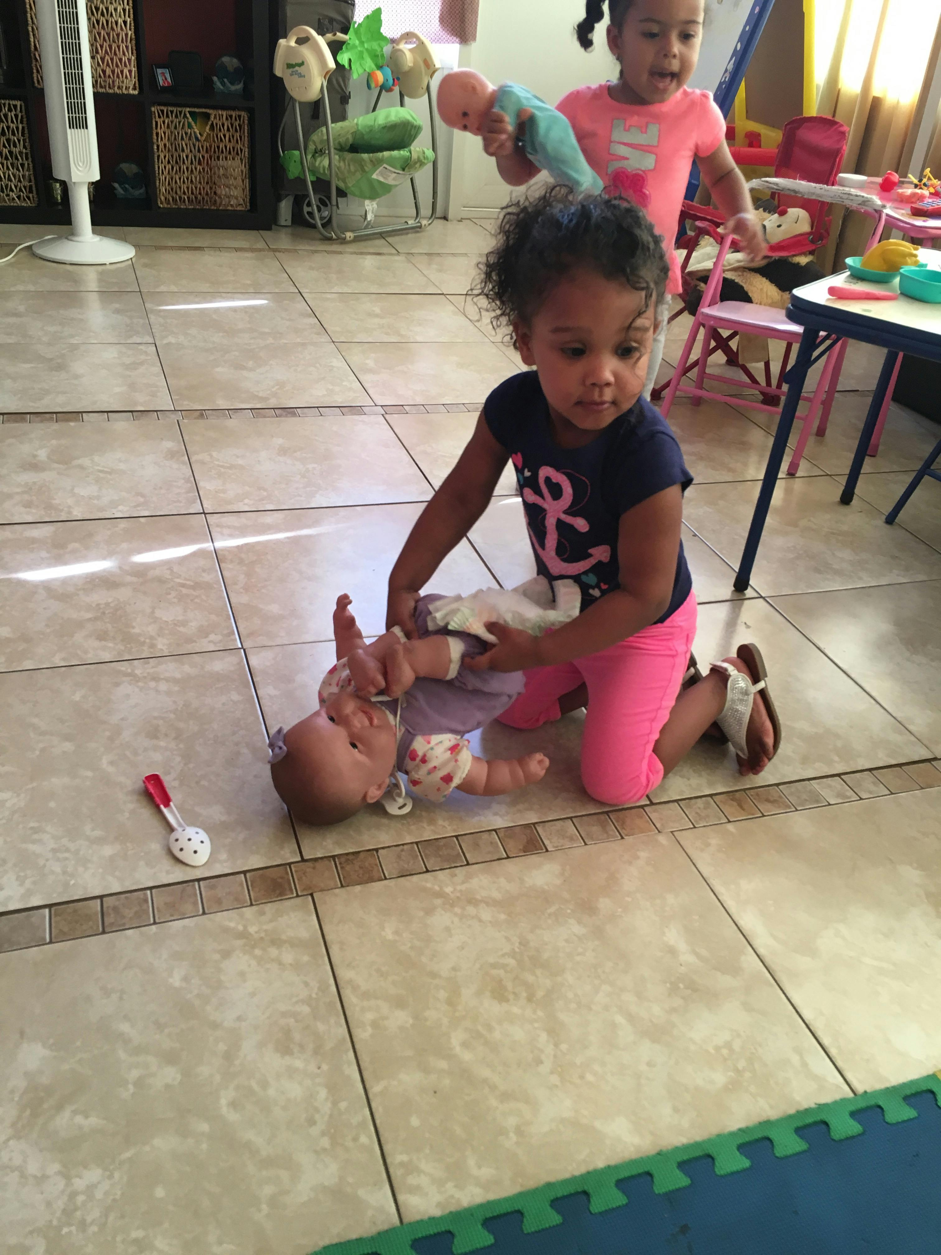 Child kneeling on a tiled floor playing with a doll