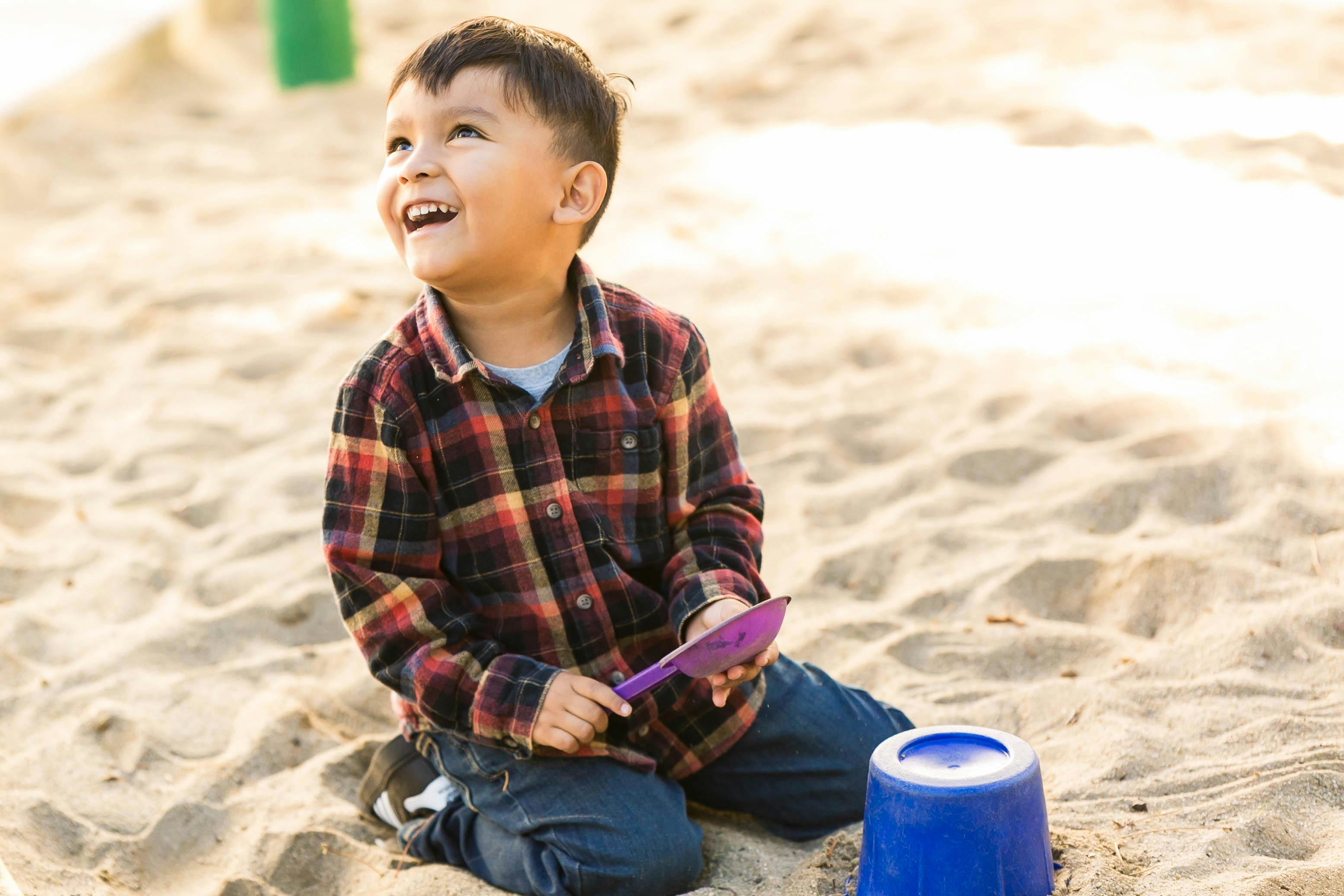 Child kneeling in sand with a shovel and bucket