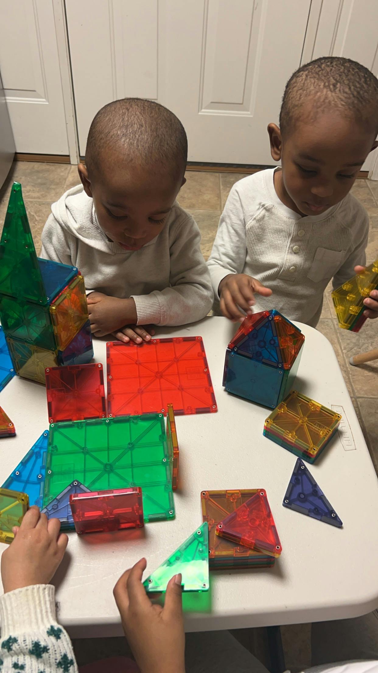 Two children playing with colorful magnetic building tiles on a table