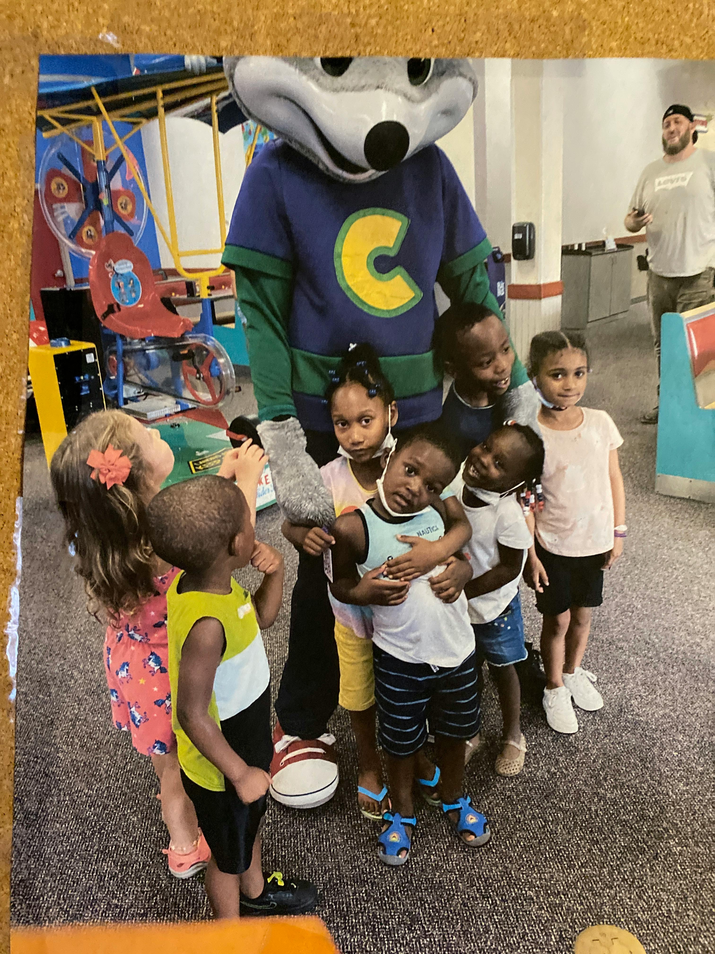 Mascot in a blue shirt with a yellow C surrounded by children