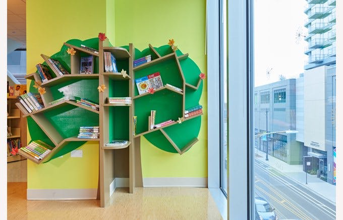 Tree-shaped bookshelf with books on a yellow wall next to a large window