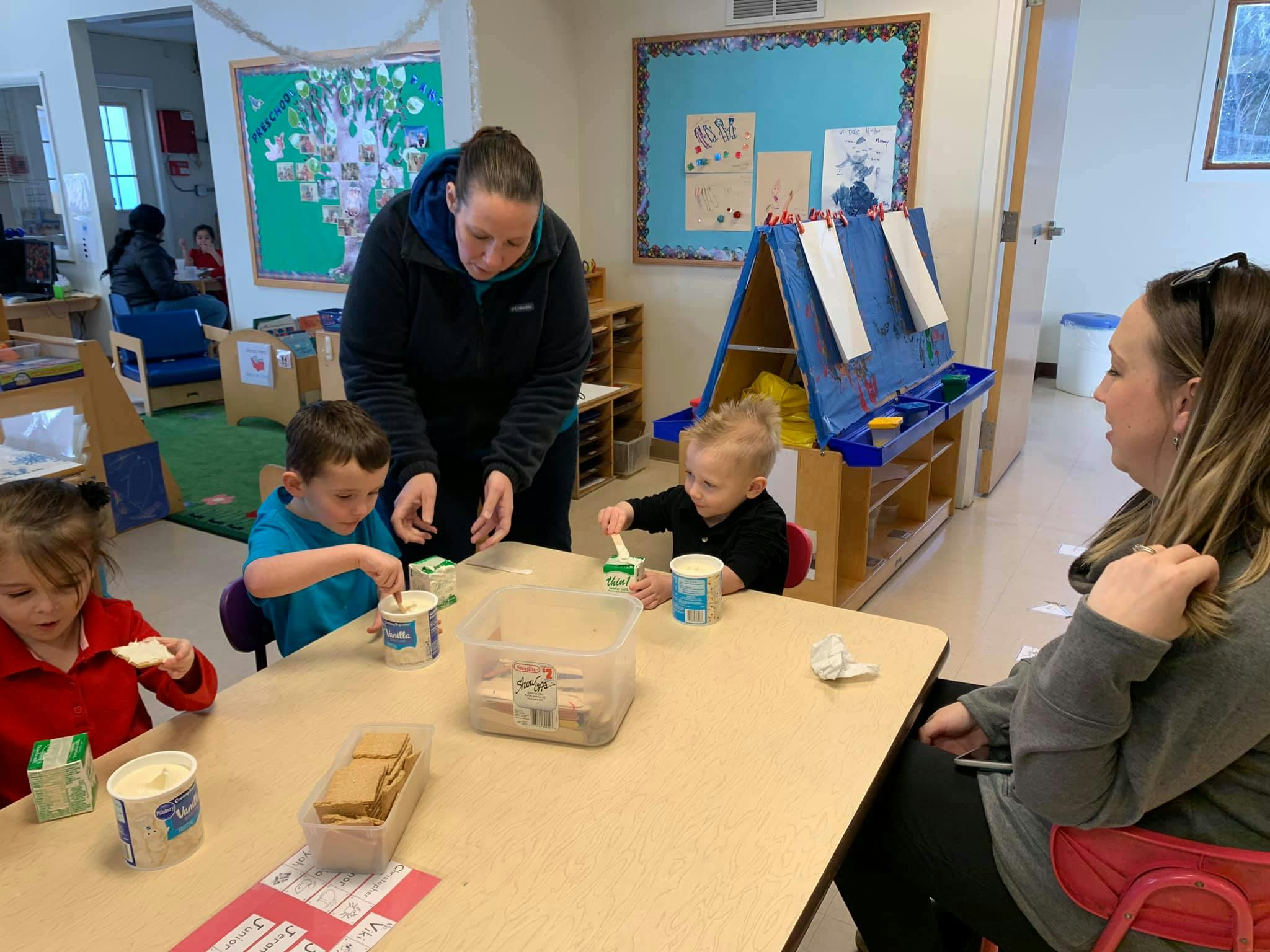 Adults and children at a table eating snacks in a classroom
