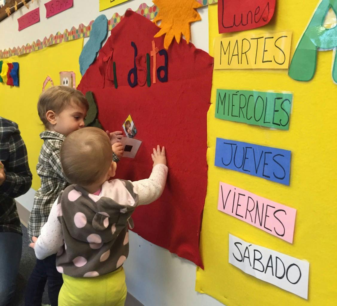 Two children interacting with a red felt board and a yellow board with Spanish days of the week