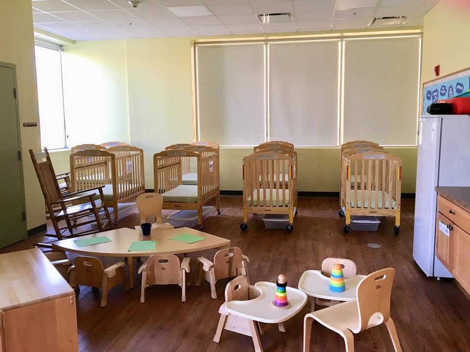 Daycare room with multiple cribs, small tables, and chairs
