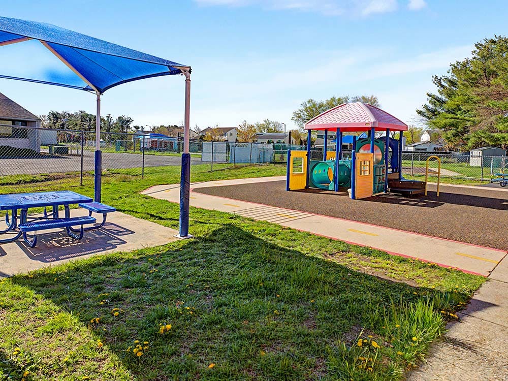 Playground with blue picnic table under a shade structure and colorful play equipment