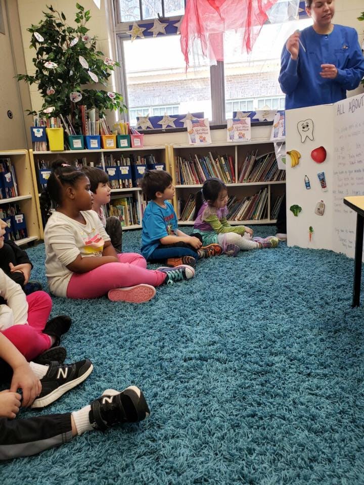 Adult speaking to children sitting on a rug in a classroom