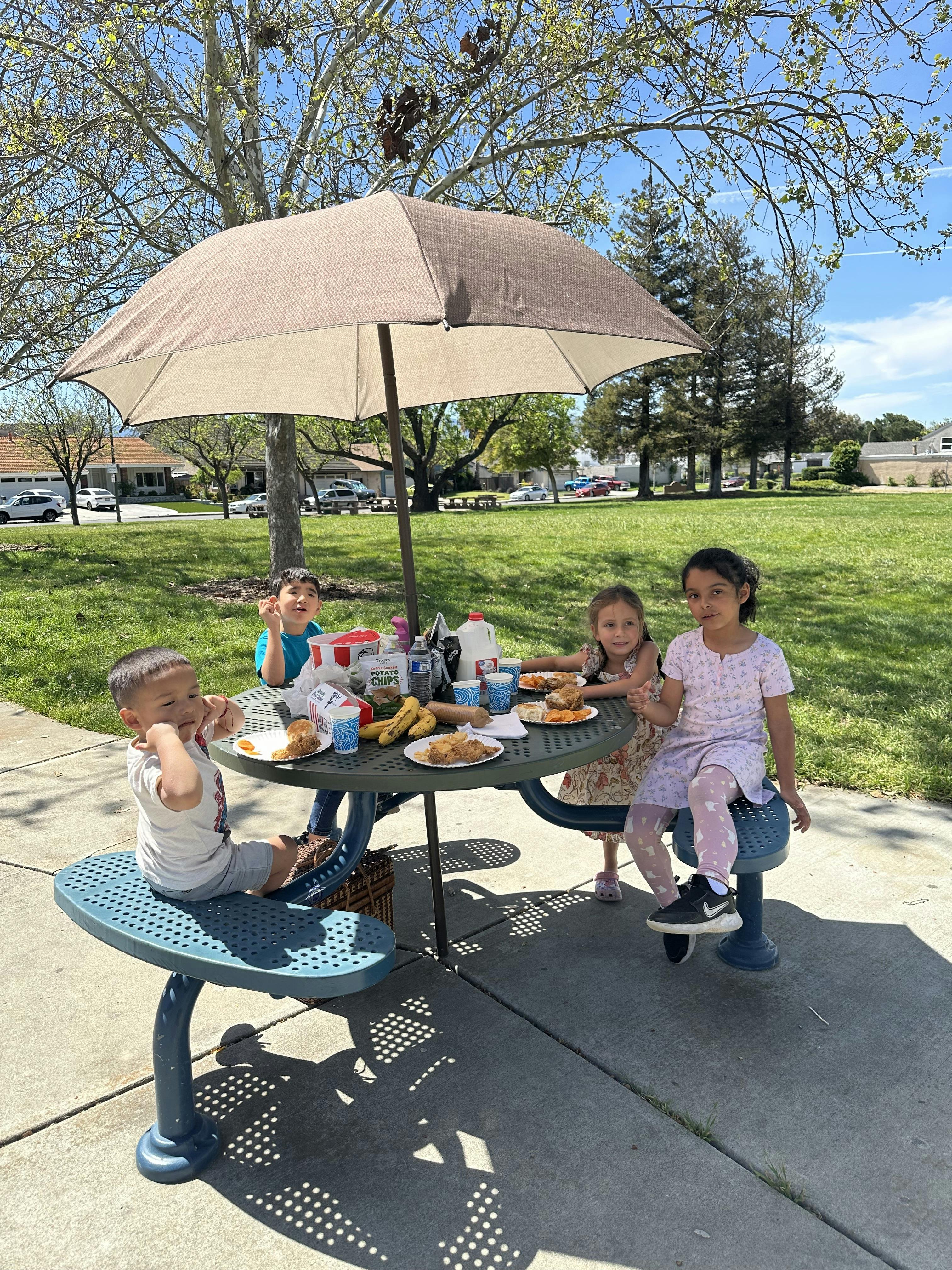 Children eating at a picnic table under an umbrella