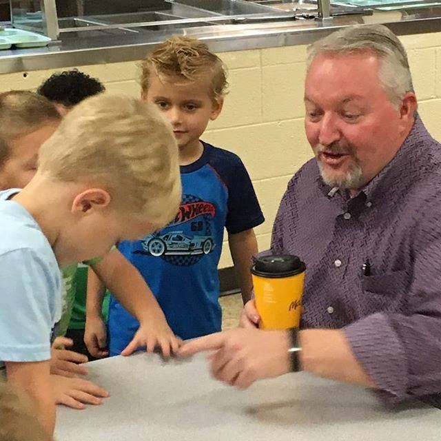 Adult person pointing at a child's hand, other children watching
