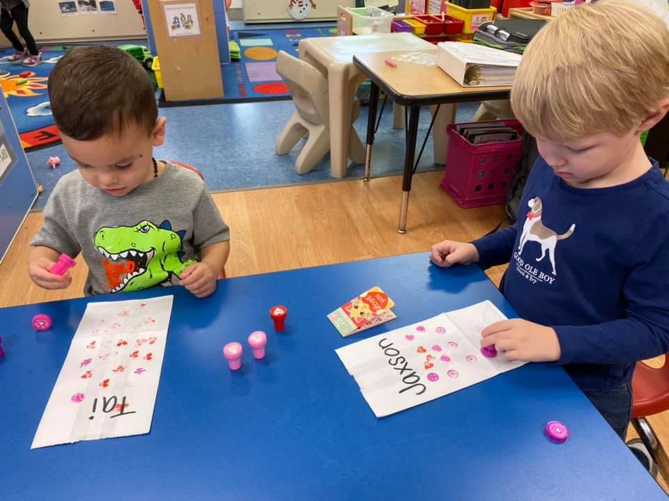 Two children at a blue table with papers and small pink objects
