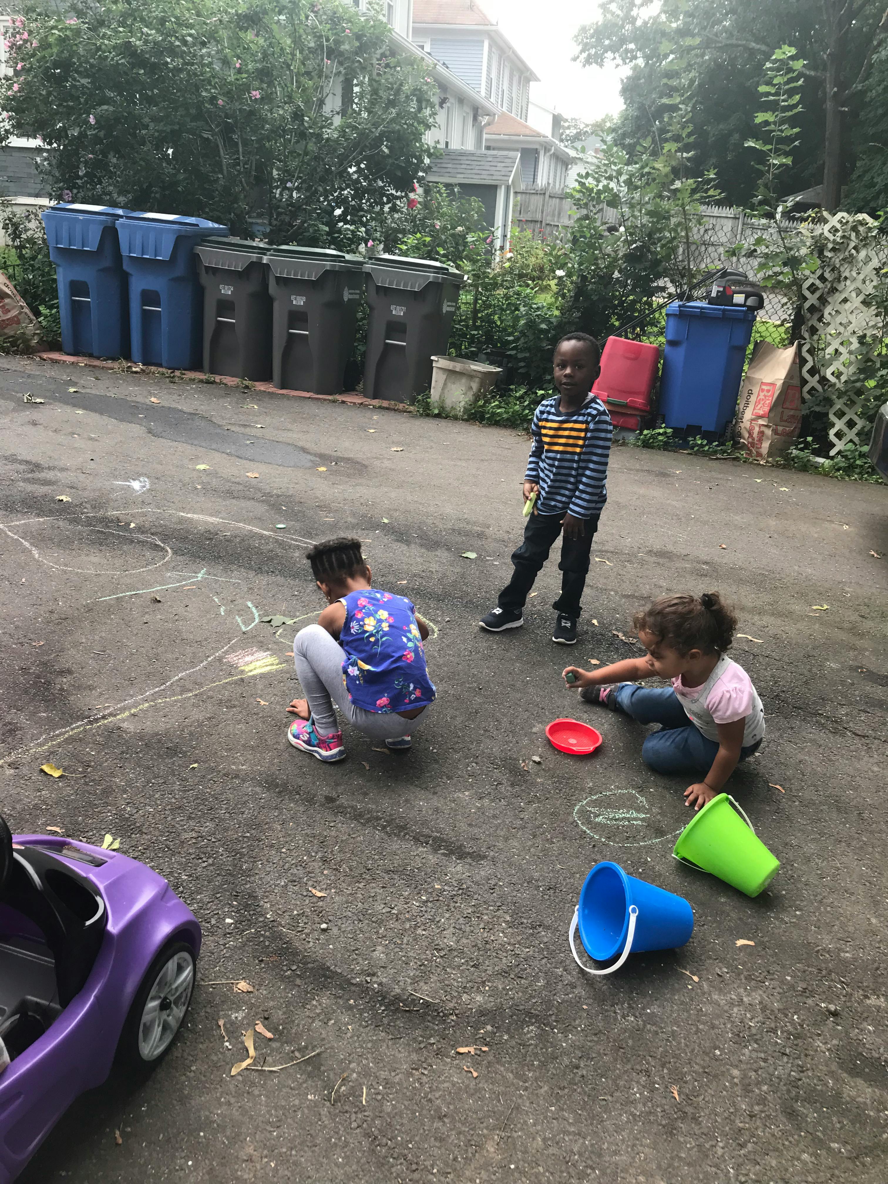 Three children drawing with chalk on pavement