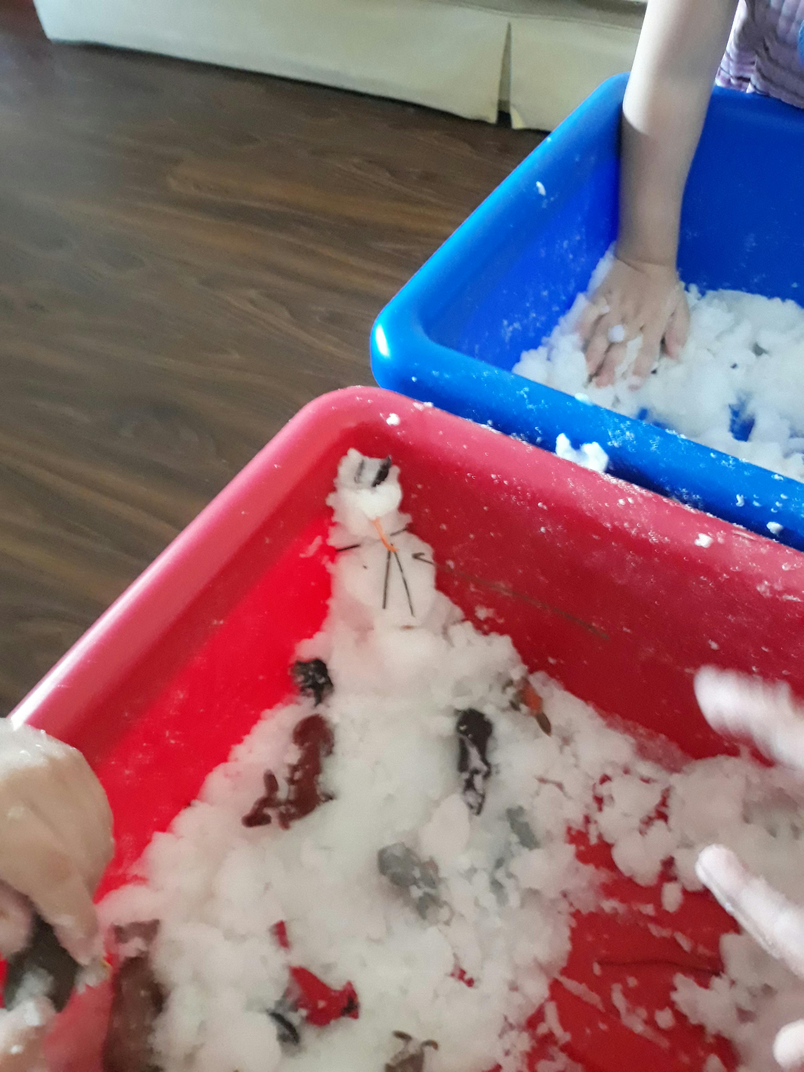 Children playing with snow in red and blue bins