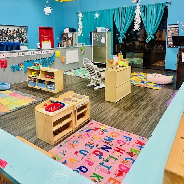 Playroom with wooden toy kitchen, shelves, and colorful rugs