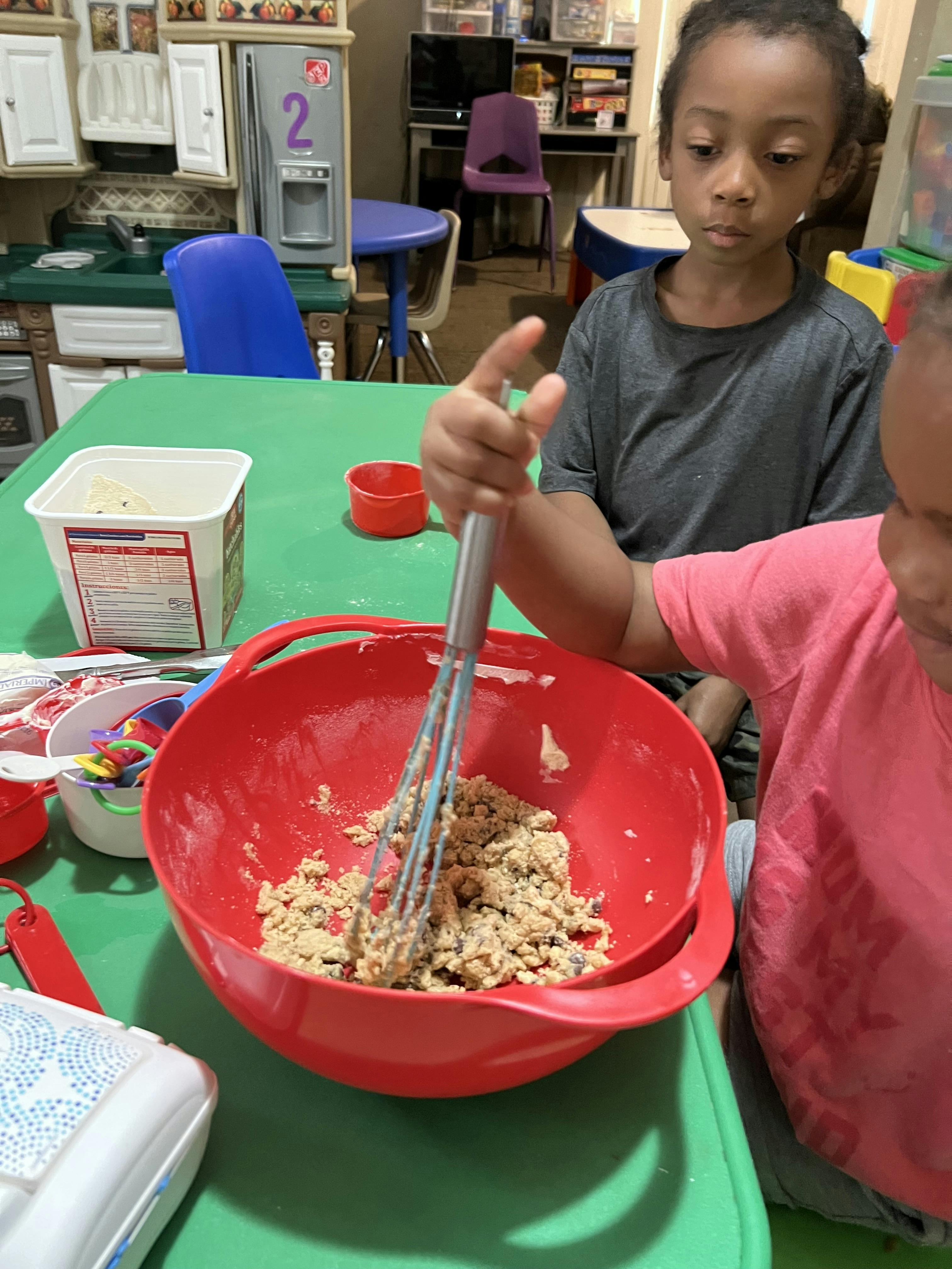 Child mixing cookie dough in a red bowl with a whisk