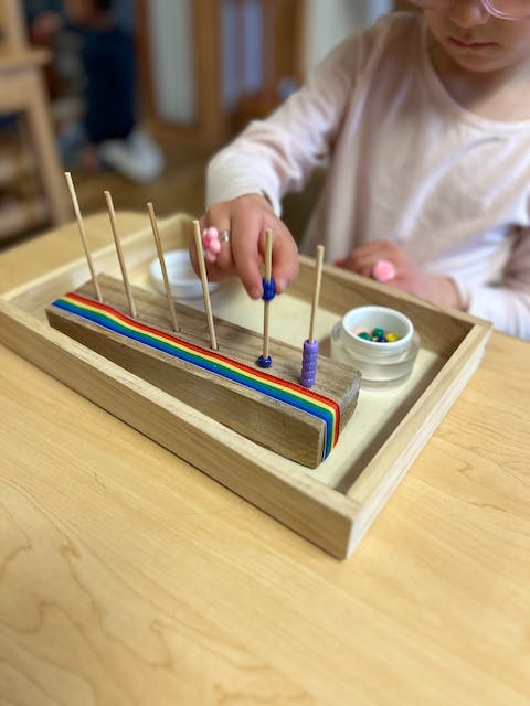 Child's hands placing beads on a wooden counting toy with rainbow stripes