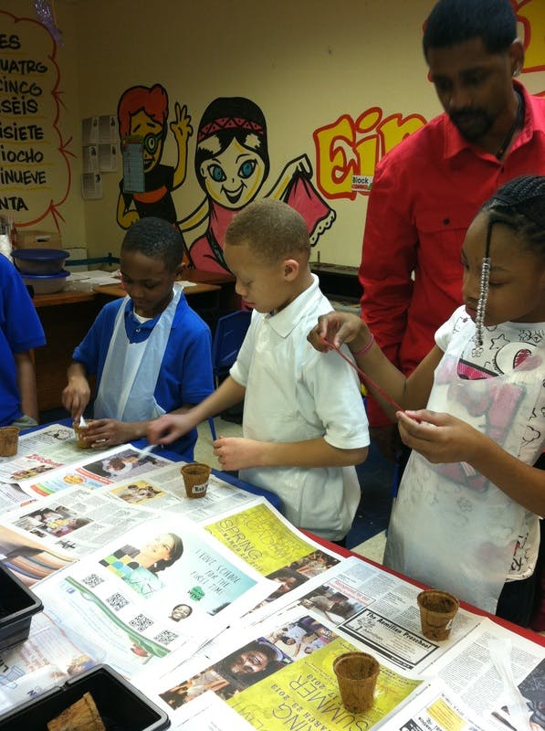 Adult and children planting seeds in small pots on a newspaper-covered table