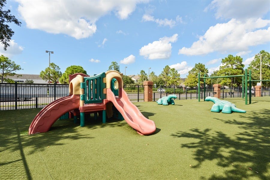 Playground with slides, climbing structure, and dinosaur statues on artificial turf