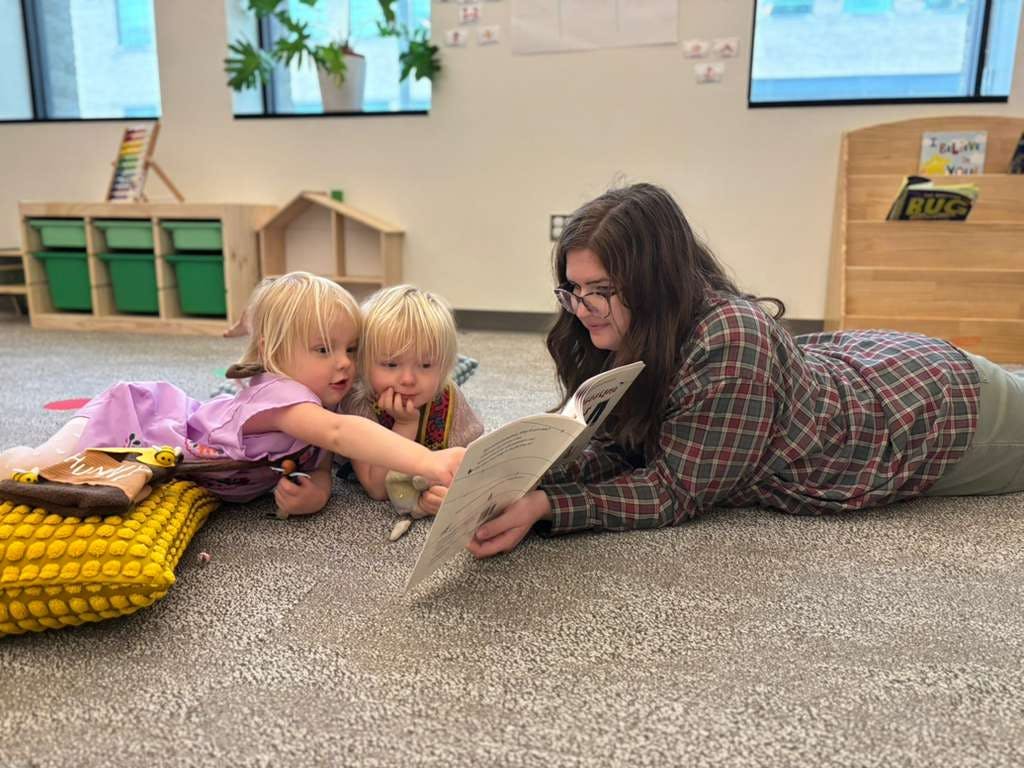 Adult and two children reading a book together on the floor of a classroom
