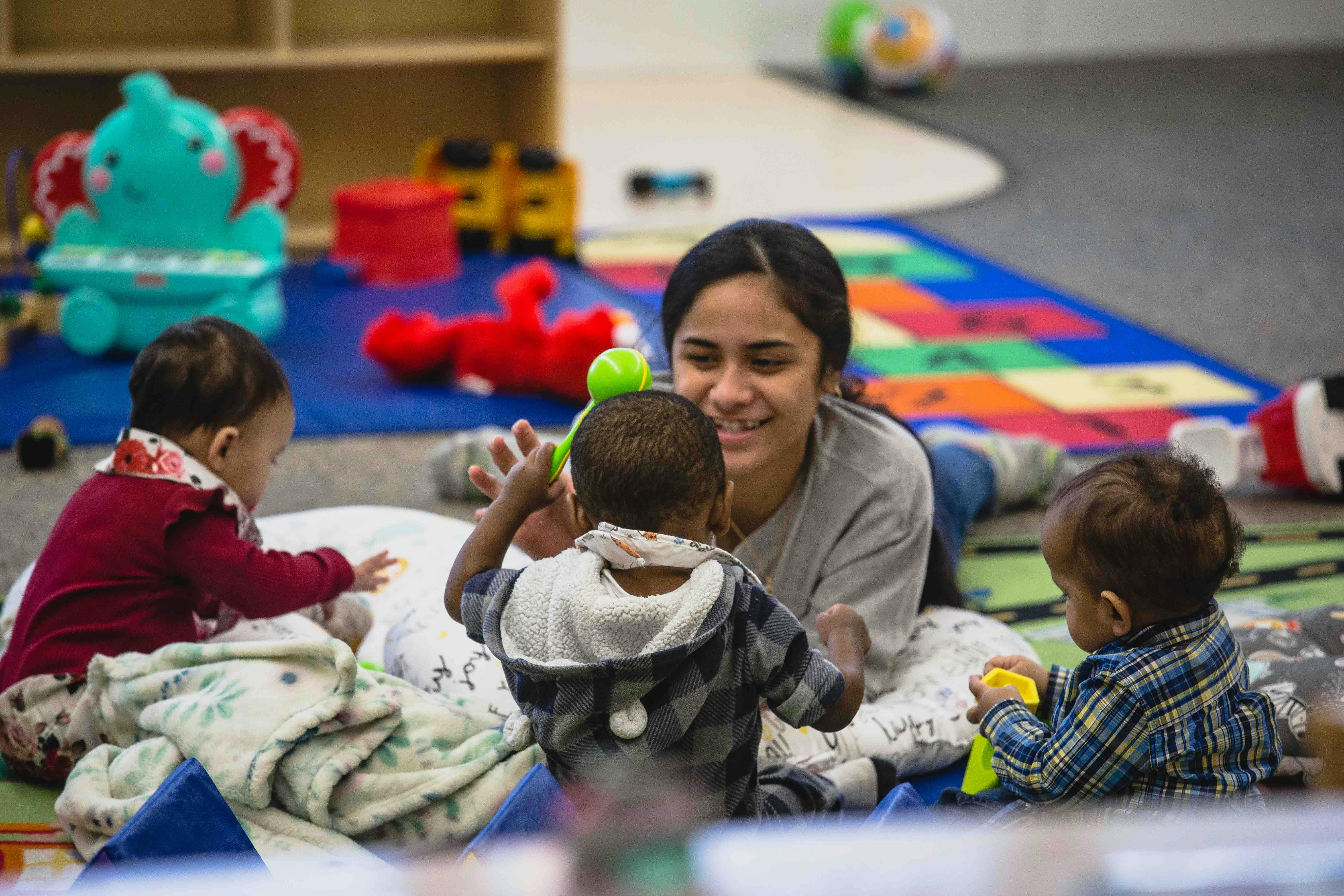 Person playing with three children on a colorful mat in a room