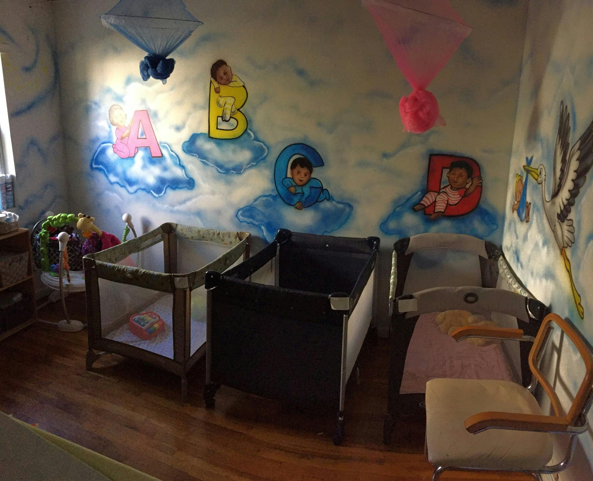 Nursery room with three cribs and a wall mural of letters and babies