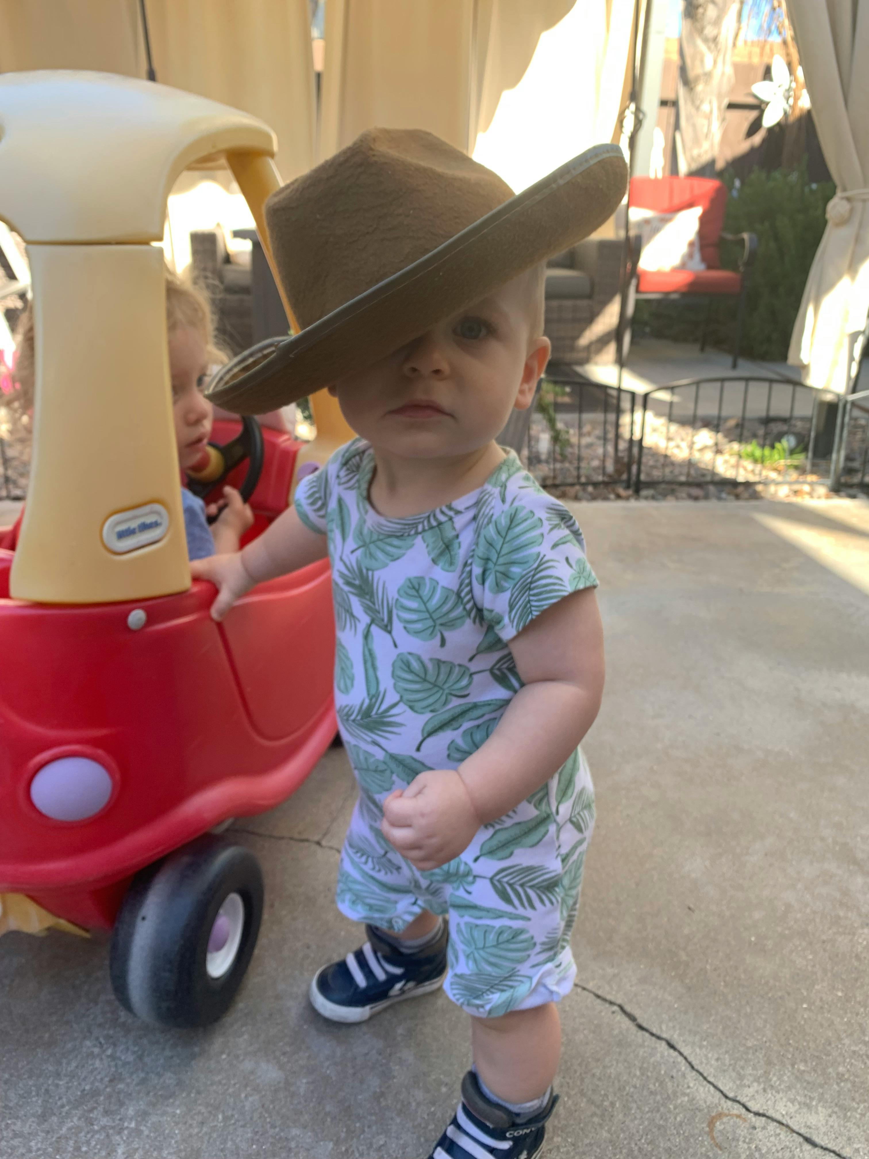 Child wearing a hat standing next to a toy car