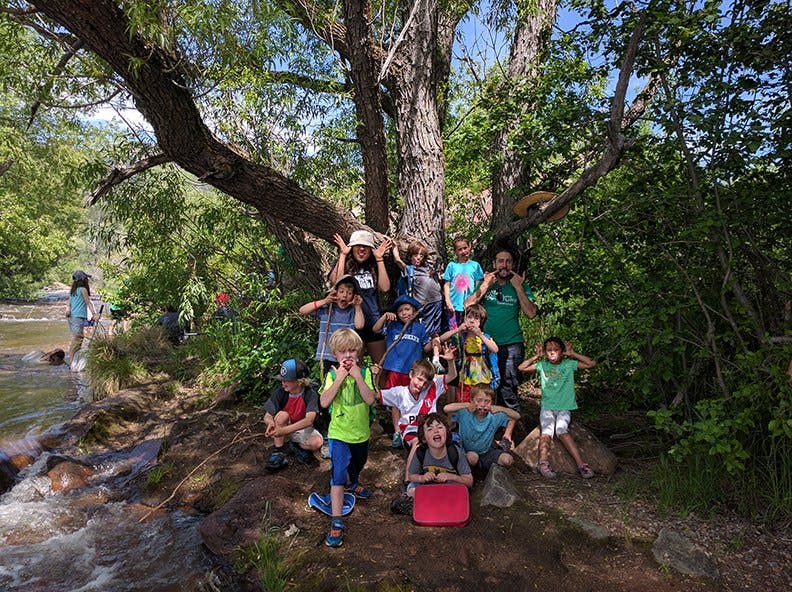 Group of children making funny faces under a large tree by a stream