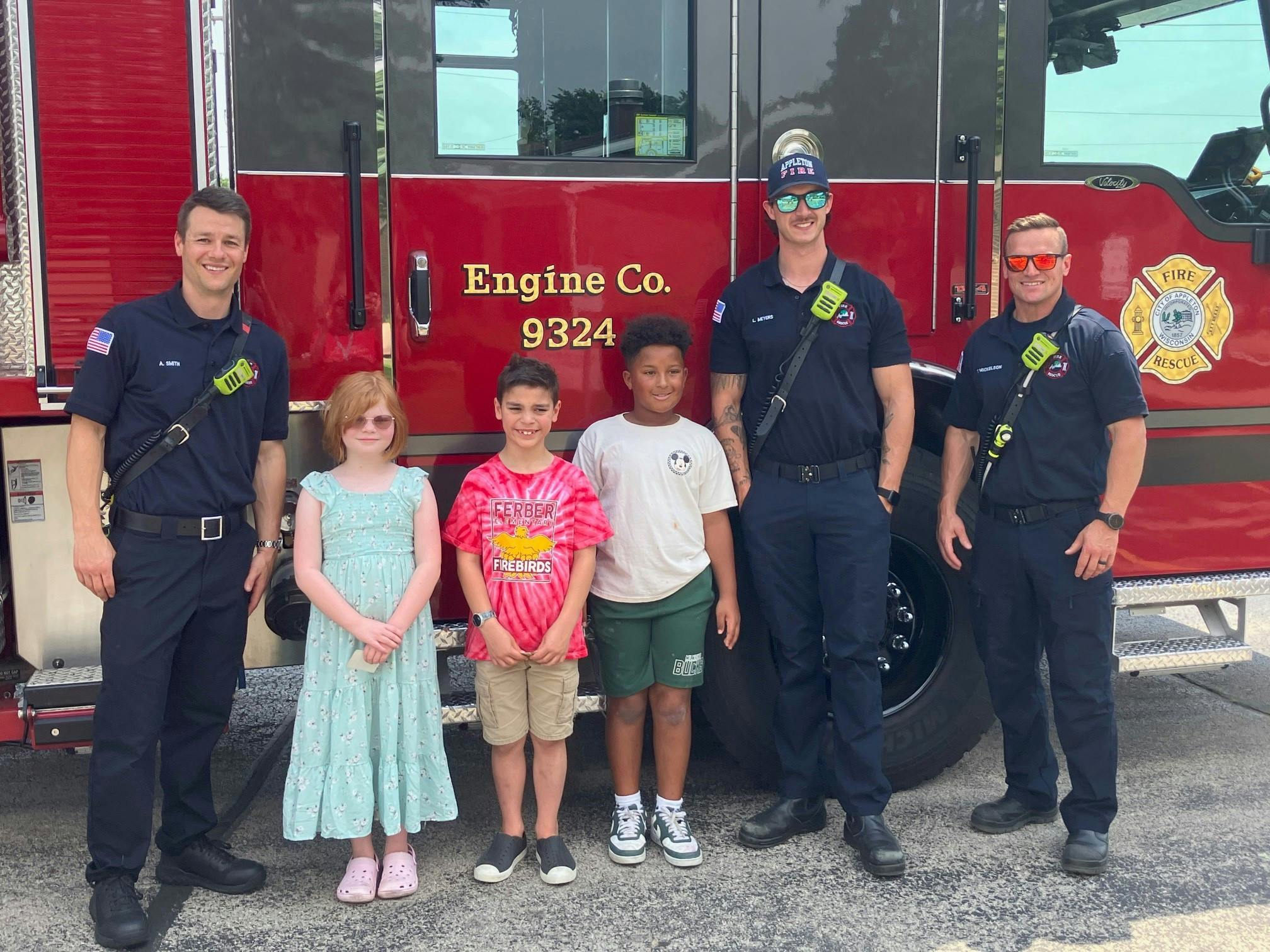 Three adults and three children standing in front of a fire truck