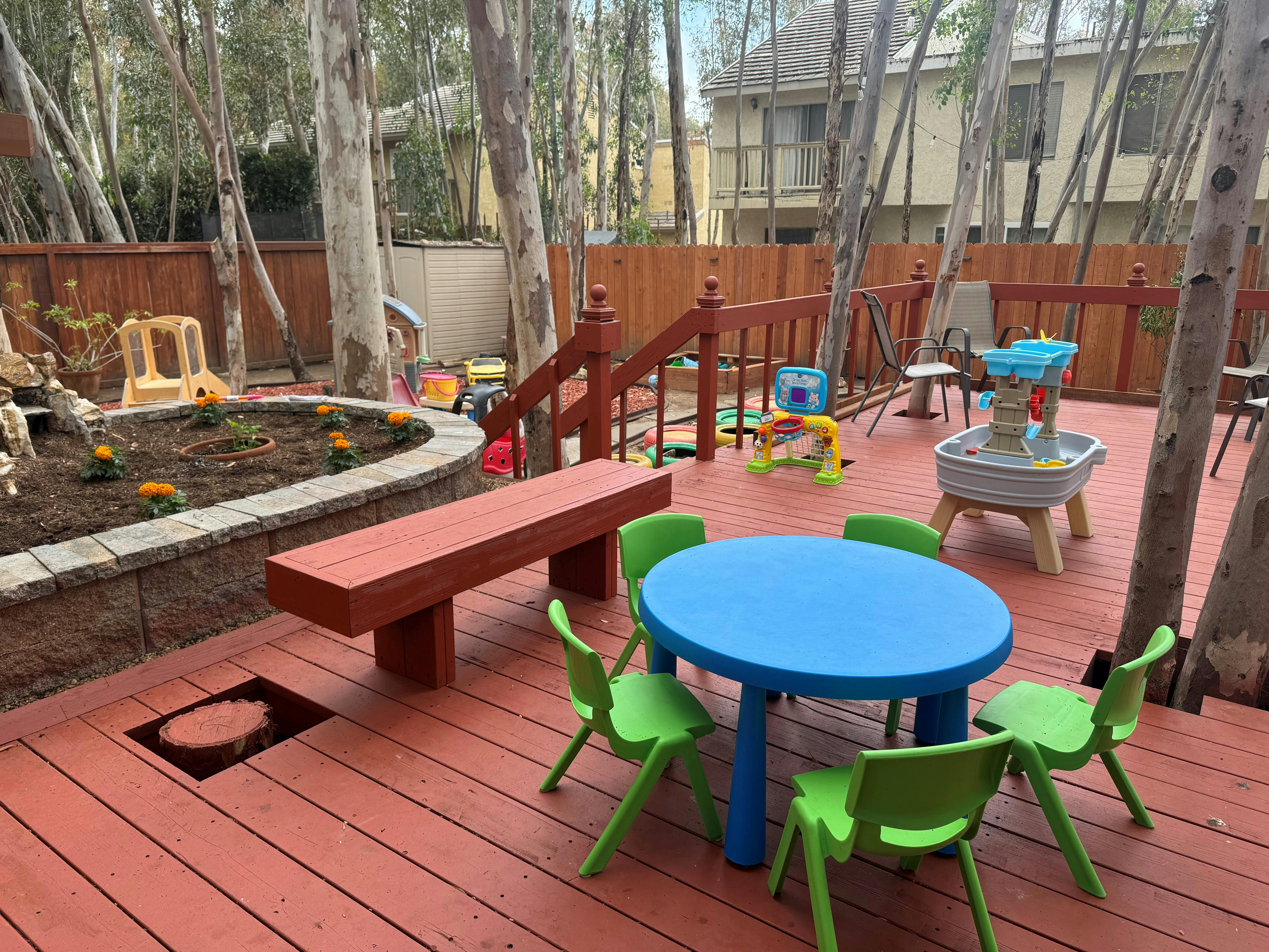Outdoor play area with a blue table, green chairs, and a wooden deck