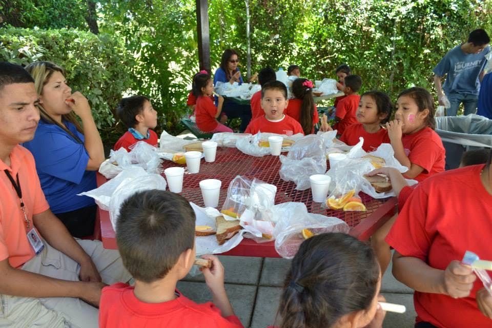 People and children eating at a picnic table outdoors