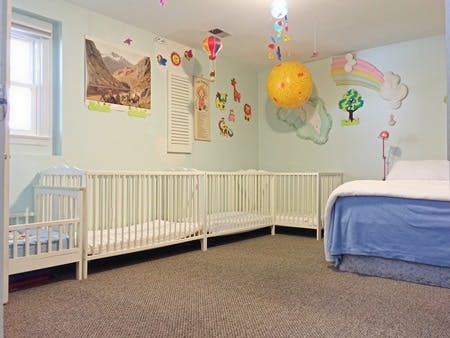 Nursery room with multiple white cribs and a bed