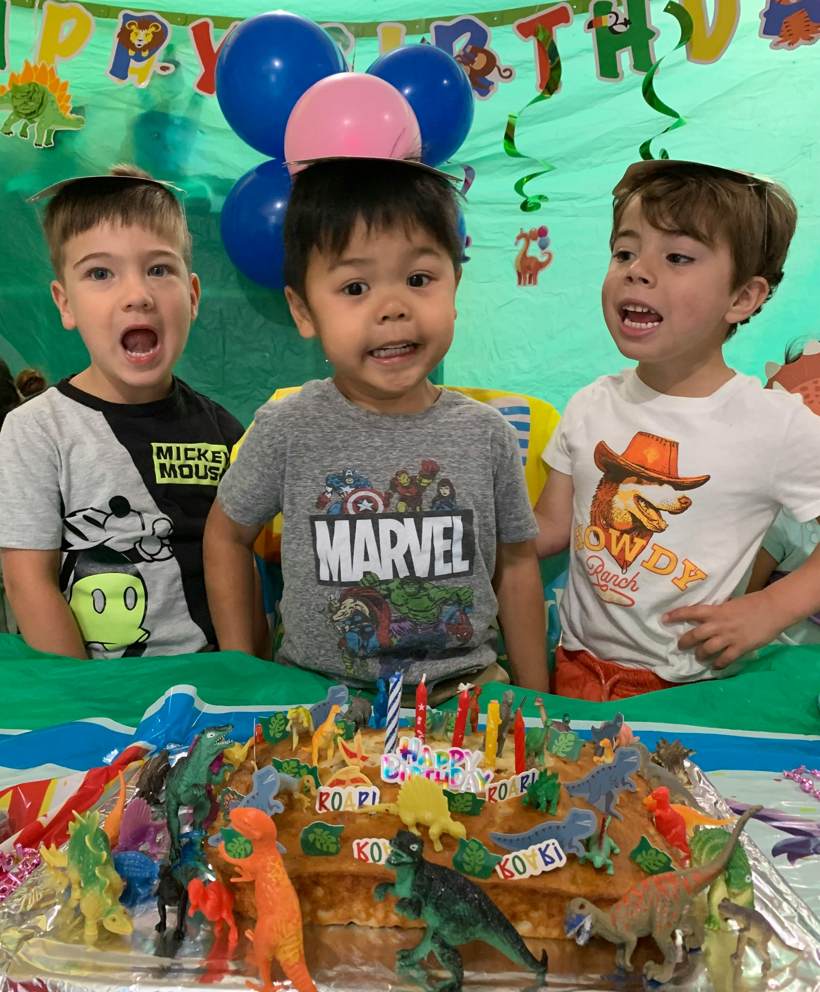 Three children behind a dinosaur-themed birthday cake