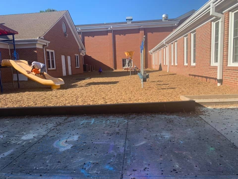 Child on a yellow slide in a playground area next to a brick building