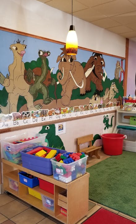 Classroom with cartoon animal mural, alphabet chart, and toy storage shelves