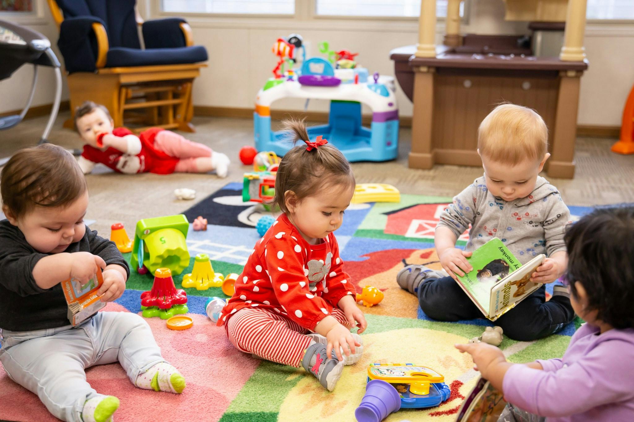 Four children playing with toys and books on a colorful rug