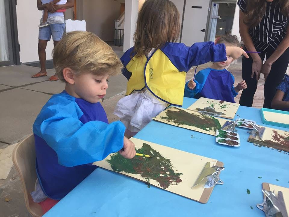 Child painting on a clipboard at a table with other children